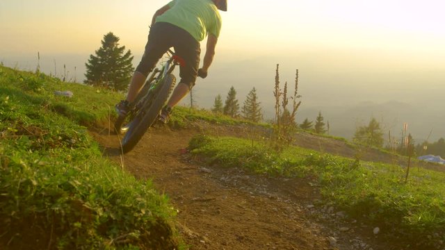 LENS FLARE, SLOW MOTION: Four mountain bikers ride into a sharp turn of a dirt path on a sunny spring evening. Golden sunbeams shine on active tourists riding their downhill bicycles along a trail.