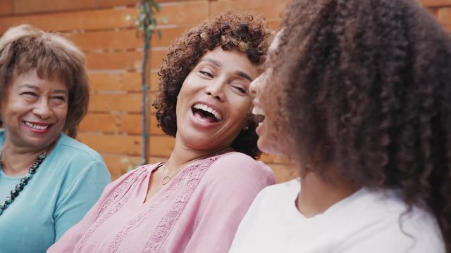 Three generations of female family members talking and laughing together outdoors, close up