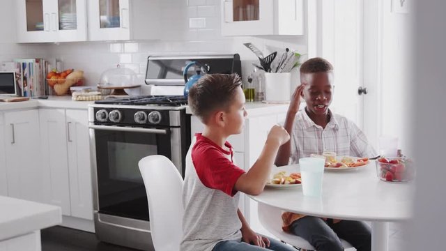 Two pre-teen male friends sit talking in the kitchen during a playdate at one boy&rsquo;s house
