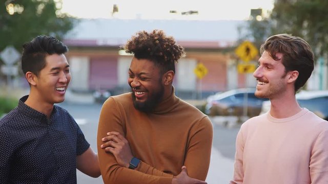 Three young adult male friends standing in a city street smiling to camera, front view, close up