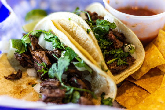 Two carne asada tacos with cilatro and onion on corn tortillas.