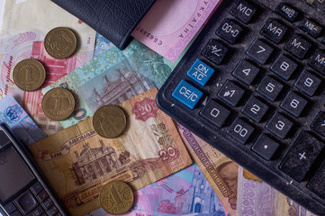 Ukrainian hryvnia, various coins. Dusty calculator, old mobile phone and black wallet. Old and new bills. Cash.