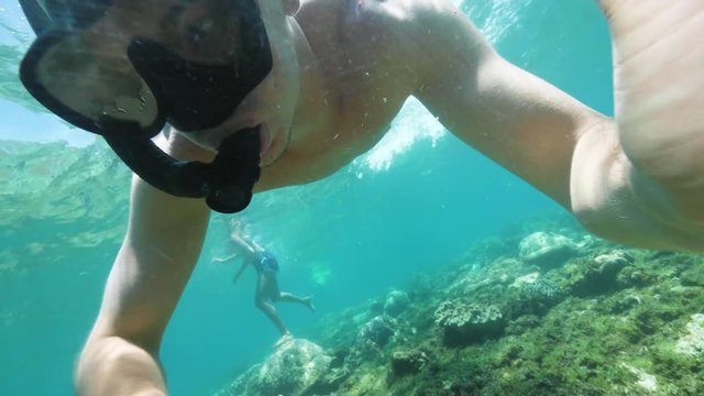Teenager boy is snorkeling in ocean floor with coral reefs, underwater shot.