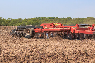 The tractor plows the soil with a cultivator smashing clods in the beds and preparing the field for spring sowing