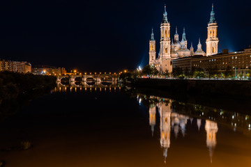 Fototapeta na wymiar Cathedral-Basilica of Our Lady of the Pilar in Zaragoza, Spain with a reflection on the river and the bridge that cross it