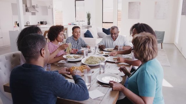 Three generation black family sitting at dinner table serving spaghetti, elevated view