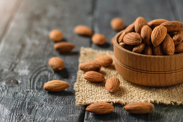 Almonds in a wooden bowl on a piece of burlap on a dark wooden table.