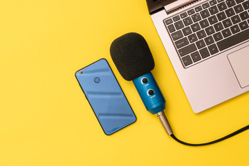 Blue and blue smartphone microphone near the laptop on a yellow background. The concept of...