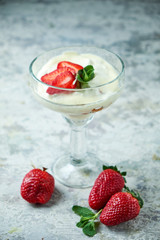 Ice cream with strawberries in a glass vase. Gray textured background. Dessert