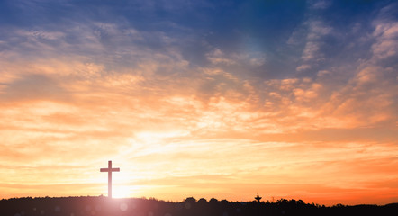 black cross religion symbol silhouette in grass over sunset or sunrise sky