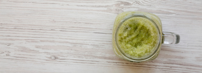 Glass jar mug filled with green celery smoothie on a white wooden background, top view. Overhead, flat lay. Copy space.