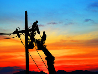 Silhouette Electrical engineers working on electricity pylon high tension power line repairs and maintenance  on blurry sunset background