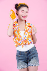 The girl holds a bottle of orange juice on a pink background.