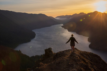 gender neutral hiker silhouetted against mountain backdrop overlooking lake at sunset