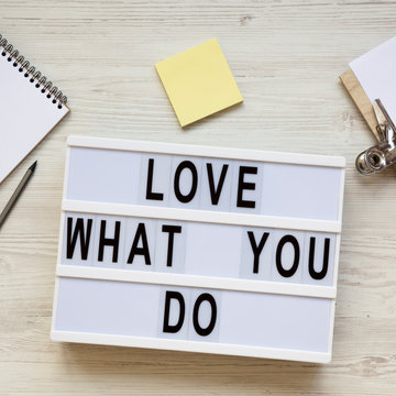 Modern board with text 'Love what you do', notepad, pencil and noticepad over white wooden background, top view. Business concept. From above, flat-lay, overhead.