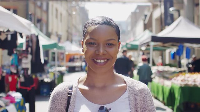 Portrait of young black female in a street market smiling to camera, in slow motion