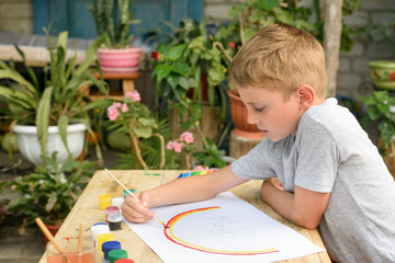 Cute boy draws rainbow. Open air. Garden in the background. Creative concept. © somemeans