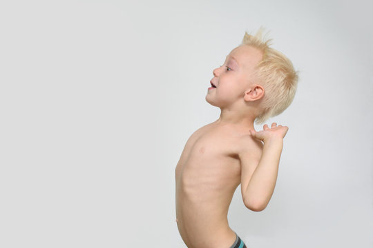 Surprised little blonde shirtless boy depicts a strong wind. Profile. White background. Summer concept
