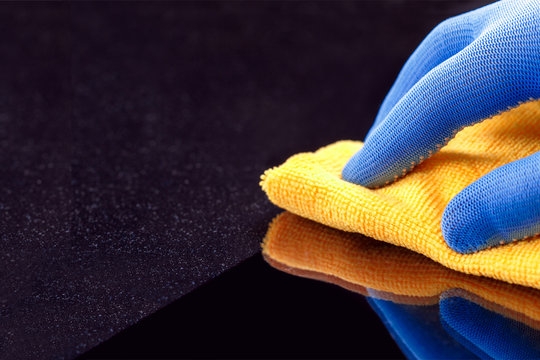 Hand in protective glove wiping dust layers on the furniture  with yellow dry rag. General or regular cleanup. Commercial cleaning company. Copy space.