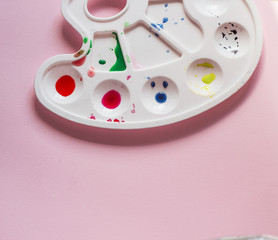 white plastic palette with paints on a pink background, artist tool