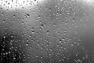 Raindrops on glass in rainy weather close up. Natural background black and white