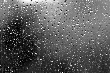Raindrops on glass in rainy weather close up. Natural background black and white
