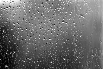Raindrops on glass in rainy weather close up. Natural background black and white