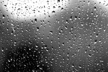 Raindrops on glass in rainy weather close up. Natural background black and white