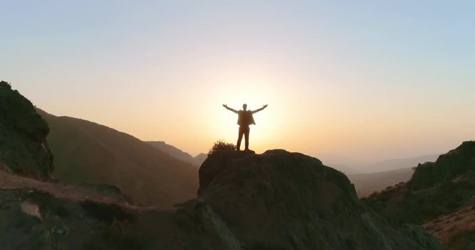 successful businessman standing on top of a mountain, victoriously raising his hands up - way to success, on top of world concept 4k aerial