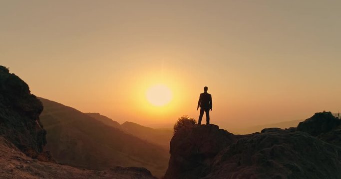 successful businessman standing on top of a mountain, victoriously raising his hands up - way to success, on top of world concept 4k aerial