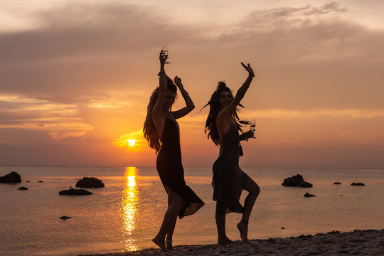 silhouette of two young beautiful girls having fun on the beach at sunset