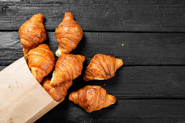 Freshly baked croissants on black wooden table, top view.