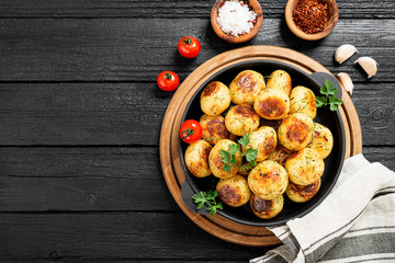 Roasted new potato in frying pan on black wooden background.