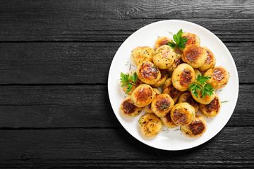 Roasted new potato in white plate on black wooden background.