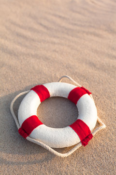 Retro Life Preserver at Holiday Sand Beach / Nostalgic miniature life buoy with rope and red stripes on wavy beach sand background (copy space)