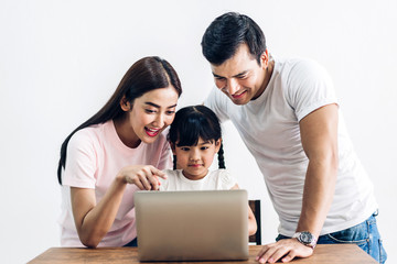 Fototapeta premium Happy family father and mother with daughter sitting and looking at laptop computer together in the living room at home