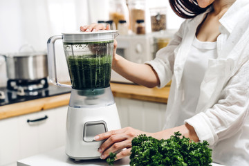 Healthy woman enjoy making green vegetables detox cleanse and green fruit smoothie with blender in...