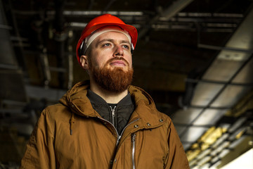 The average plan portrait of an adult man in a helmet with redhead, evaluates, studies, looks to the side, horizontal, free space for signature
