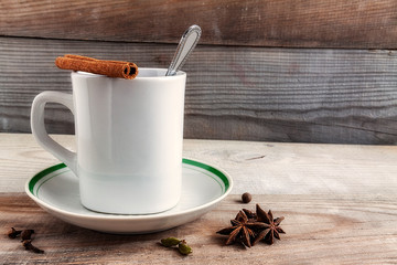 Mug with cloves cinnamon saucer teaspoon tea on a natural wooden background.