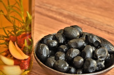 olive oil in a bottle with a sprig of razmorina and garlic, black olives on a saucer