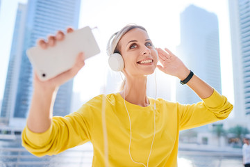 Technology and music. Happy young woman with earphones and smartphone dancing while exercising on city embankment.