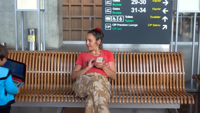 Dalaman Airport, Turkey - 24th of May 2018: 4K Mother with smartphone and son with laptop in the airport lounge