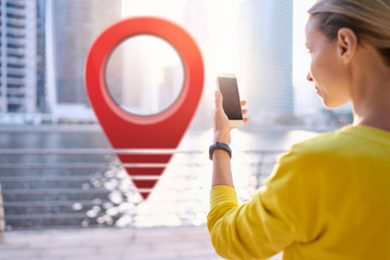 Young woman using smartphone on the city embankment with 3d red location pin GPS pointer on the...