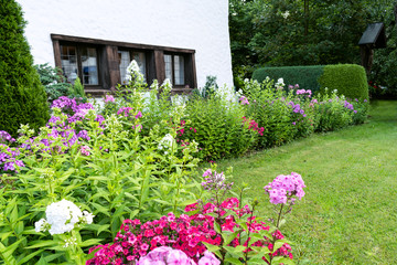 View of the well-kept garden with a green lawn, flowers and trees near the house.