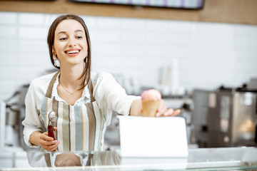 Young and happy saleswoman in apron making ice cream at the counter of the modern pastry shop indoors