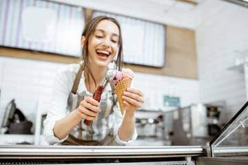 Young and happy saleswoman in apron making ice cream at the counter of the modern pastry shop...