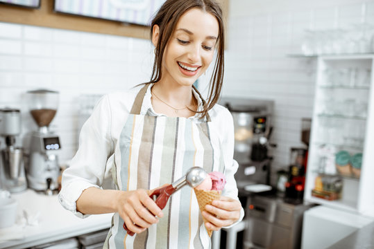 Young and happy saleswoman in apron making ice cream at the counter of the modern pastry shop indoors