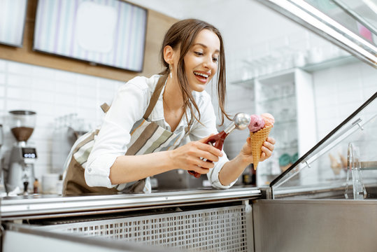Young and happy saleswoman in apron making ice cream at the counter of the modern pastry shop indoors
