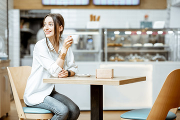 Young smiling woman drinking coffee while sitting in the modern pastry shop