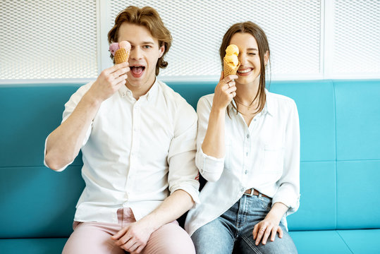 Young Couple Having Fun, Enjoying Ice Cream While Sitting Together On The Bright Sofa Indoors